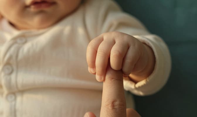 Mão de bebê segurando o dedo de um adulto